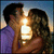 Pixelated static image of two people kissing at sunset with a bright light flare between them, set against a blue sky background.