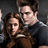 Two figures in dark clothing embrace against a gray background, with one figure's head positioned close to the other's shoulder.