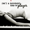A black-and-white image of a person lying on a piano keyboard, with text above reading "SHE'S A DIFFERENT KIND OF PLAYER" and small red dots scattered near the text.