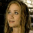 Pixelated close-up of a person with long brown hair, light skin, and neutral expression against dark background with light patches.