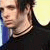 Pixelated close-up of a person with dark hair wearing a dark shirt and a silver chain necklace against a light background.