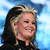 Pixelated close-up of a person with long dark hair and light streaks, smiling against a blue gradient background.