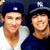 Two people wearing baseball caps with an 'NY' logo, one in a white shirt and the other in a dark blue shirt, smiling in a