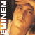 Static pixelated image of a person with orange-toned skin and dark hair, featuring vertical white text on the left side reading "EMINEM" against a black background strip.
