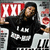 A person in a black hoodie with white text poses against a background featuring red "XXL" and piano keys.