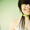 A person with short dark hair and bangs wears a green choker and white strapless top against a light green background.