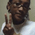 A pixelated image of a person with dark skin wearing a white shirt, making a peace sign gesture with their right hand.