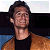Pixelated static image of a person with dark hair wearing a black tank top and brown jacket against a blurred background.