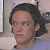 Pixelated close-up of a person with dark hair tied back, wearing a light-colored shirt against a blurred background.