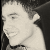 A black-and-white pixelated image of a smiling person with short hair, featuring a pink heart symbol in the top-right corner.