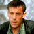 Static pixelated image of a person with short dark hair wearing a green shirt and dark jacket against a light background.