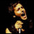 Pixelated figure in profile view holding a microphone, wearing dark clothing against a black background.