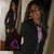 A person in a black jacket and purple shirt stands in a doorway with another person behind them, the image shifts slightly between frames.