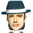 Pixelated portrait of a person wearing a dark blue fedora with a white band, light brown eyes, and a green and white checkered shirt against a gray background.