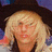Pixelated close-up of a person with light-colored hair and dark clothing against a blurred background.