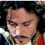 Pixelated close-up of a person with dark hair, closed eyes, and a mustache, wearing a white shirt and red garment with green accents.