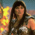 A pixelated image of a woman with long dark hair wearing a silver armored top, standing against a background with yellow and orange shapes on the left.
