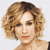 Pixelated close-up of a person with short curly light brown hair, closed eyes, and a neutral expression against a light gray background.