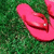 Pink flip-flops on green grass with a gray area in the bottom right corner.