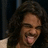 Pixelated close-up of a person with curly dark hair, open mouth showing teeth, and light-colored clothing against a dark background.