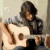 A person with dark curly hair plays an acoustic guitar in a four- , showing sequential hand movements on the fretboard and strumming motion