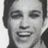 Pixelated grayscale portrait of a smiling person with short dark hair, cropped to show head and shoulders against plain background.