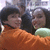 Two people in close proximity, one wearing orange clothing and the other with light-colored hair holding a green object.