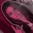 Pixelated image of a person with long dark hair holding a pink object against a maroon background.