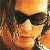 Pixelated close-up of a person wearing dark sunglasses and a light-colored shirt against a warm-toned background with orange and yellow hues.