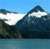 Pixelated landscape with blue sky, white clouds, dark green mountains, and light blue water.