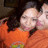 Two people in orange shirts pose closely together, one with dark hair and the other with light hair, in a pixelated image with visible motion blur.