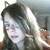Pixelated static image of a person with dark hair and light skin, wearing a dark top, against a blurred background with light and dark tones.