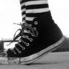 Black-and-white close-up of a high-top sneaker with striped socks, showing laces and a white rubber sole.