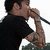 Pixelated static image of a person singing into a microphone, wearing dark clothing with visible tattoos on the arm and hand.