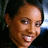 Pixelated close-up of a smiling person with short dark hair, brown skin tone, and visible teeth against a blurred background.