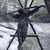 A pixelated black insect-like figure with multiple legs stands against a blurred background of light and dark gray tones.