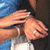 Pixelated image of two hands clasped together against a blue and dark background, with visible skin tones and partial clothing.