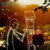 Pixelated static image with warm orange and brown tones, featuring indistinct shapes and a blurred background with hints of light and dark areas.