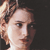 Pixelated close-up of a person's face with light brown hair, showing partial profile view against dark background.