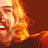 Pixelated static image of a person's face with warm orange and yellow tones against a dark brown background, appearing to be from an older digital animation or low-resolution source.