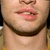 Close-up of a person's lower face showing lips, nose, and beard with a neutral expression against a blurred background.