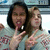 Two people pose together in a light blue shirt with red patterns, making peace signs against a blurred background.