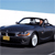 Pixelated image of a dark blue convertible car with a yellow license plate, driver visible, against a light blue sky and white horizon line.