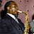 A pixelated image of a person in dark clothing playing a saxophone against a muted pink background.