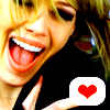 A close-up of a person with light brown hair making a playful expression, tongue out, and holding a white speech bubble with a red heart.