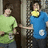 Two pixelated figures stand side-by-side against a dark background; one wears green, the other blue with yellow accents.