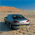 A blue car with red taillights is positioned on a sandy beach under a clear blue sky, viewed from a low angle.