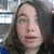Pixelated close-up of a person with long dark hair, light skin, and visible facial features against a blurred background with light and dark areas.