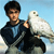 A person in a dark jacket and light shirt holds a white bird against a light blue background.