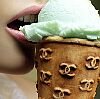 Static close-up of a person's mouth eating an ice cream cone with repeated Chanel logos on the waffle cone and green-topped scoop.